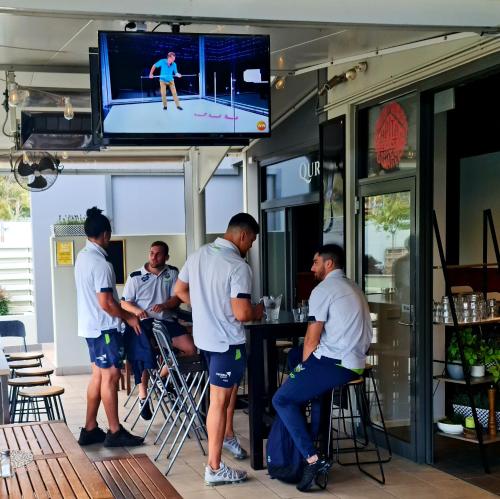 un grupo de hombres parados alrededor de un bar con TV en Qure Restaurant and Apartments Canberra Bruce en Canberra