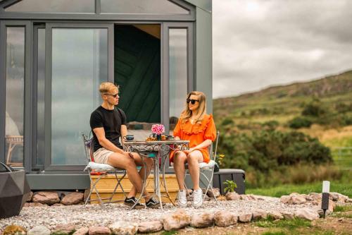 a man and woman sitting at a table outside of a caravan at Oaklane Glamping Cabins in Kenmare