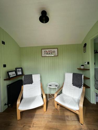 two white chairs in a room with green walls at Hettie Luxury shepherds hut in Semley