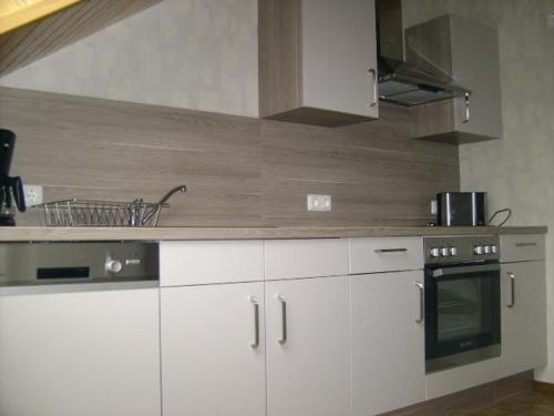 uma cozinha com armários brancos e um forno com placa de fogão em Ferienwohnung-Freuen em Blankenheim