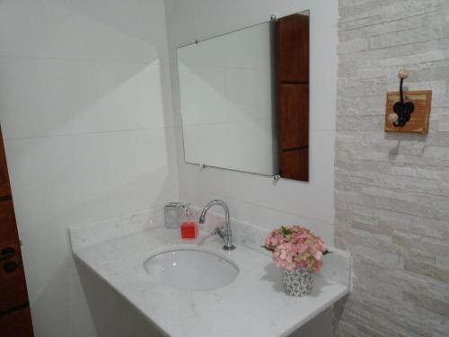 een wastafel in de badkamer met een spiegel en een vaas met bloemen bij Casa de Campo Recanto Têto in Espirito Santo Do Pinhal