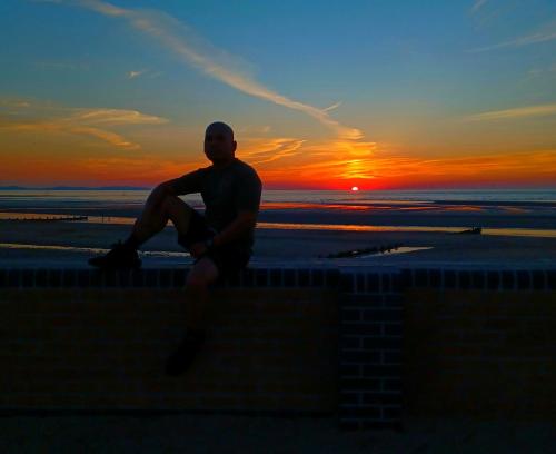 a man sitting on a ledge with the sunset in the background at Gabriel Guesthouse in Rhyl