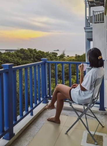 a woman sitting in a chair on a balcony at Chelona Beachfront Huahin in Khao Tao