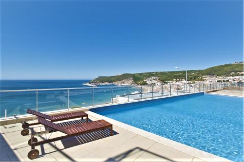 - une piscine avec deux bancs à côté de l'océan dans l'établissement Sesimbra Sunshine Cliffs, à Sesimbra