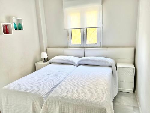 ein weißes Bett in einem weißen Schlafzimmer mit einem Fenster in der Unterkunft MI CAPRICHO BEACHFRONT- 3-7 Apartment with sea views in Mijas Costa