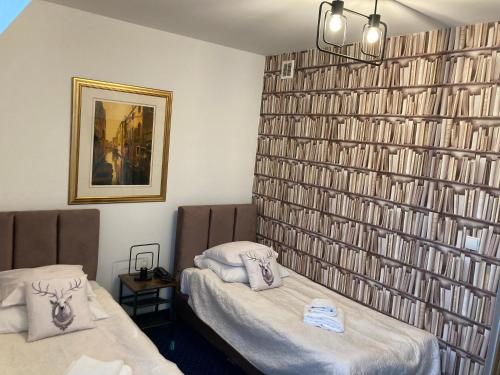 two beds in a room with a wall of books at Hotel Bella in Jelenia Góra