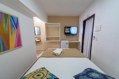 um quarto com uma cama branca e uma televisão em Praia do Forte Suites na Praia do Forte