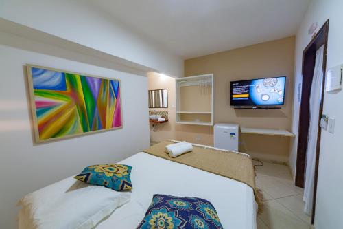 um quarto com uma cama e uma televisão de ecrã plano em Praia do Forte Suites na Praia do Forte