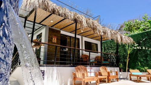 a house with a straw roof with chairs and a table at Shark Town Mal Pais in Santa Teresa Beach