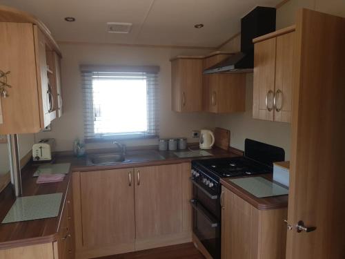 een keuken met houten kasten, een fornuis en een raam bij 6 Berth Caravan on Lakeside Holiday Park in Burnham on Sea