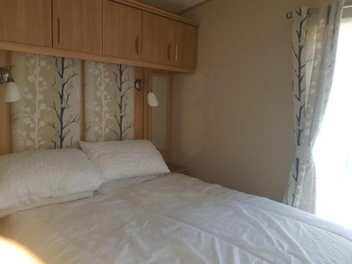 Schlafzimmer mit einem Bett mit weißer Bettwäsche und einem Fenster in der Unterkunft 6 Berth Caravan on Lakeside Holiday Park in Burnham on Sea