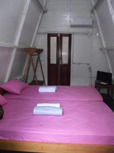 a pink bed with two white towels on it at Tanjong Tinggi Cottage in Sijuk