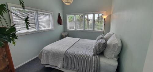 a bedroom with a bed and two windows at Quintessential kiwi bach in Oneroa