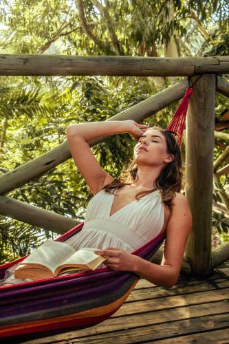 a woman laying on a hammock with a book at Otentic, Eco Tent Experience in Grande Rivière Sud Est