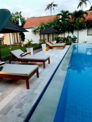 a swimming pool with chaise lounges and tables next to a house at The Edicha in Lovina