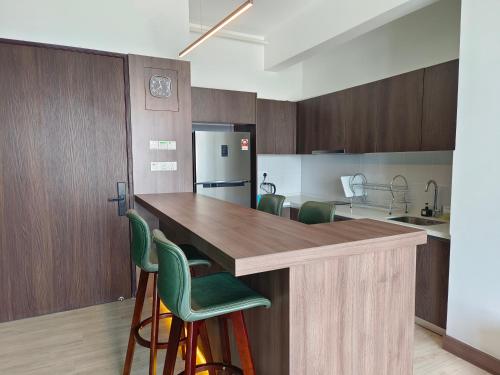 a kitchen with a large wooden counter with green chairs at One Bedroom Troika Kota Bharu by AGhome in Kota Bharu