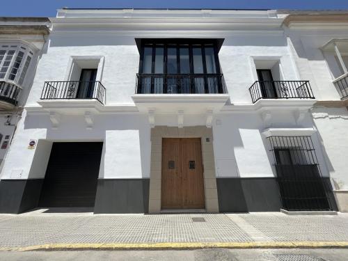 een wit gebouw met een houten deur en 2 balkons bij CAMASanlúcar in Sanlúcar de Barrameda