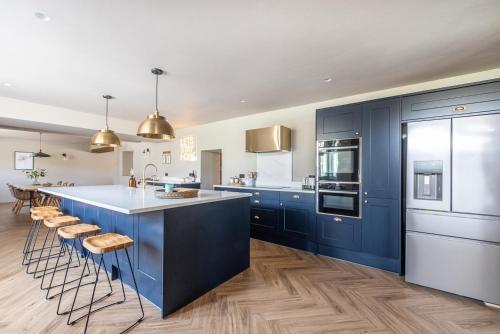 uma cozinha com armários azuis e uma ilha de cozinha com bancos em Immaculate 6 Bed House - Unique Cellar Bar- Airbnb em Warminster