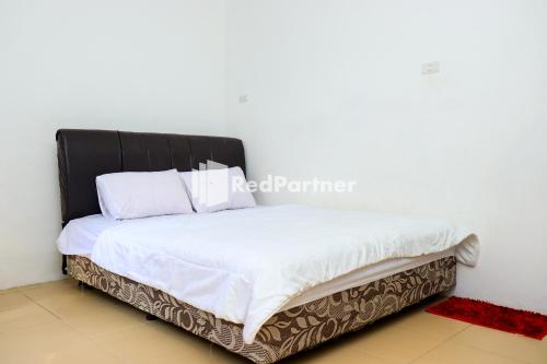 uma cama com lençóis brancos e uma cabeceira preta em Sahabat Pantai Guest House Mitra RedDoorz em Tanjungbinga
