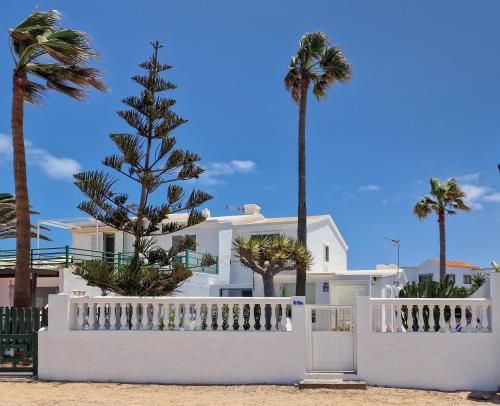 a white house with palm trees and a white fence at Villa La Maja Beachfront in Corralejo