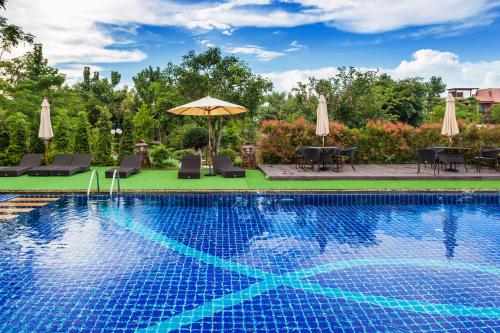 a swimming pool with chairs and an umbrella at Phukumhom Khao Yai in Wangkata