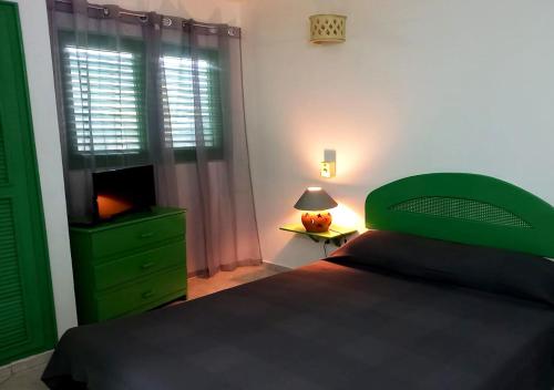 a bedroom with a green bed and a table with a lamp at Residence Nord Est in Las Terrenas