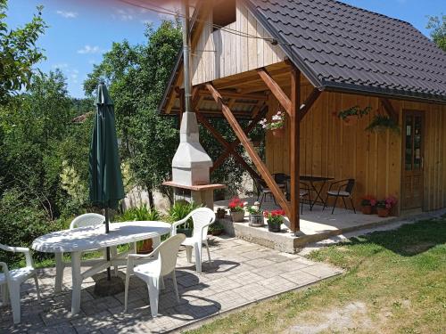 ein Haus mit einem Tisch, Stühlen und einem Sonnenschirm in der Unterkunft Kuća za odmor Lešnica in Brod na Kupi