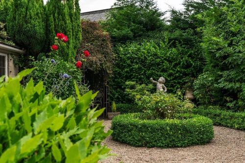 a garden with a statue and flowers and bushes at Lovedays Cottage, A Luxury 16th Century home in Painswick in Painswick