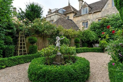 a statue of a girl in a garden in front of a house at Lovedays Cottage, A Luxury 16th Century home in Painswick in Painswick