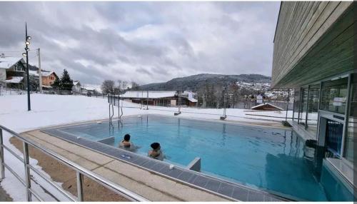 2 personnes dans une piscine dans la neige dans l'établissement Appartement moderne près du lac et centre ville. Résidence les Eaux Vives., à Gérardmer