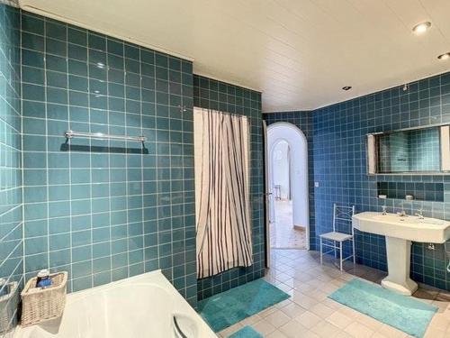 a blue tiled bathroom with a tub and a sink at Vakantiehuis Clarys in Veurne