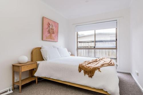 a white bedroom with a bed and a window at Seascape at The Cape in Cape Paterson