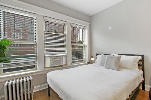 - une chambre avec un grand lit blanc et des fenêtres dans l'établissement Stylish Studio Apartment in Portage Park - Pensacola 2N, à Chicago
