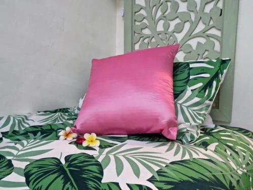 a pink pillow on a bed with green leaves at Red Palms in Blahbatu