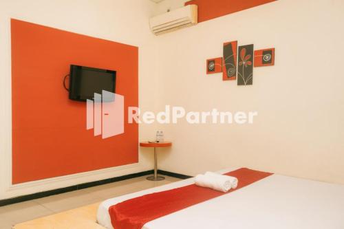 - une chambre avec une cloison rouge, un lit et une télévision dans l'établissement Pits Hotel Mitra RedDoorz near Atom Mall, à Gembong