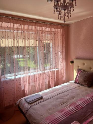 a bedroom with a bed and a window with pink curtains at Hotel DANIELA in Nīca