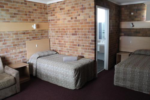 a room with two beds and a brick wall at Tally Ho Motor Inn in Tenterfield