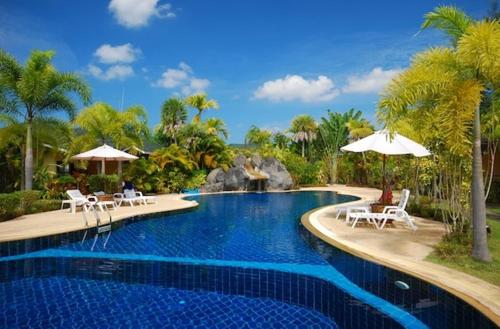 a pool with chairs and umbrellas in a resort at Palm Garden Resort in Khao Lak