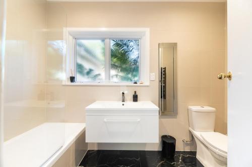 a white bathroom with a sink and a window at Grange Harbour View B&B in Tauranga