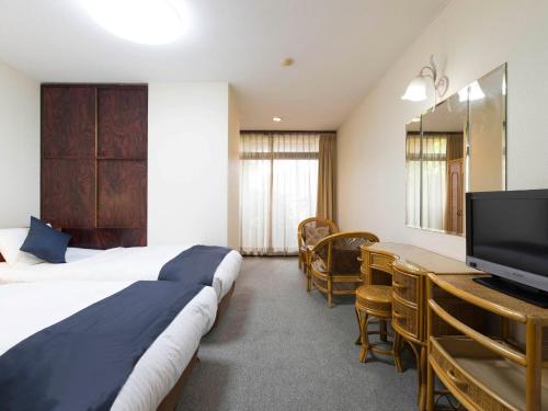 a hotel room with a bed and a television at Tabist New World Hotel Kagoshima Kanoya in Kanoya