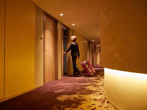 a woman walking down a hallway with a suitcase at Hotel Metropolitan Saitama-Shintoshin in Saitama