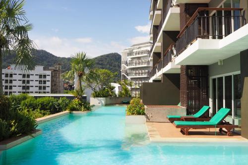 une piscine avec deux chaises et un bâtiment dans l'établissement Andakira Hotel - SHA Extra Plus, à Patong Beach