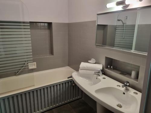 La salle de bains est pourvue d'un lavabo, d'une baignoire et d'un miroir. dans l'établissement Hotel Le Comty, à Feurs