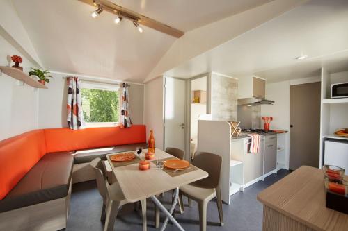 a kitchen and living room with an orange couch and a table at Camping Le Beaulieu in Puilboreau