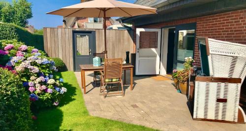 a patio with a table with an umbrella and some flowers at Hues-Stroongoedj-Haus-Strandgut in Westerland (Sylt)