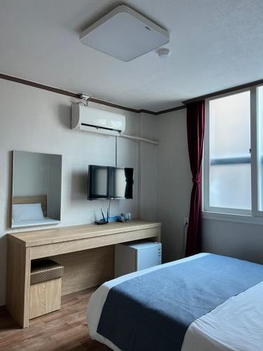 a bedroom with a bed and a desk with a television at Bricks Stay Jeju City & Aiport in Jeju