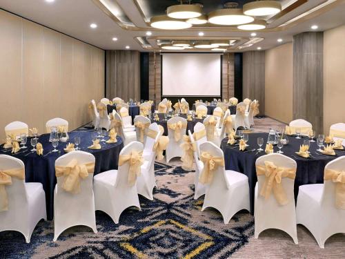 a conference room with tables and chairs and a screen at Mercure Makassar Nexa Pettarani in Makassar