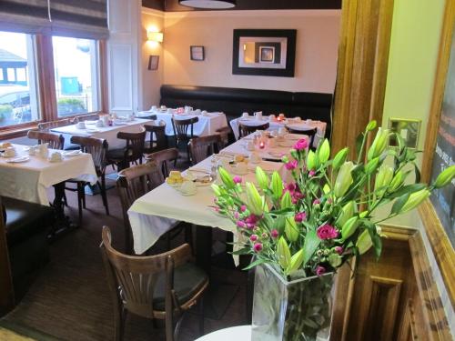 uma sala de jantar com mesas brancas e flores num vaso em The Spinnaker Hotel em Gourock