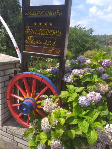 a sign with a red wagon wheel next to some flowers at Apartmani Mali Raj Rudnik in Rudnik Kačerski