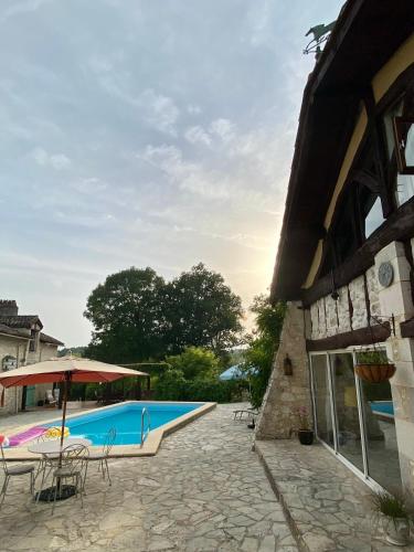 a swimming pool next to a building with a table and an umbrella at Anahata Gite in Constant